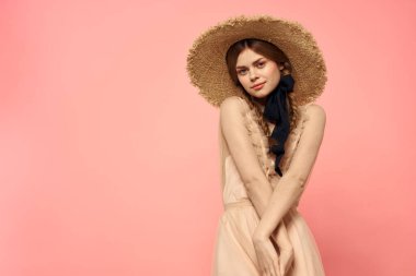 Pembe arka planda siyah kurdeleli şık elbiseli ve şapkalı bir kadın model duygularının eğlenceli görüntüsünü kırptı.