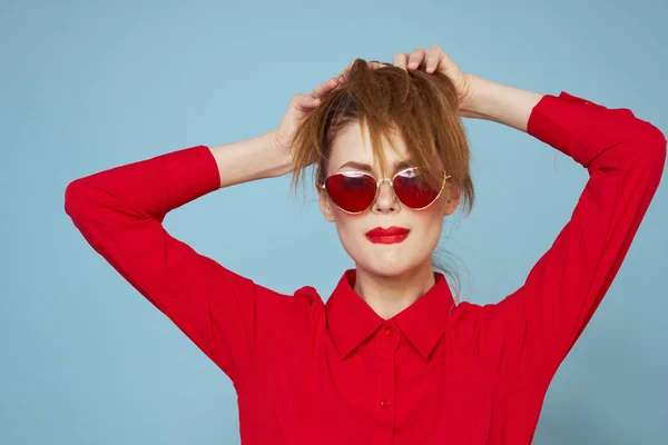 Donna in camicia rossa su sfondo blu tiene le mani vicino al viso e occhiali da sole modello di trucco labbra rosse — Foto Stock
