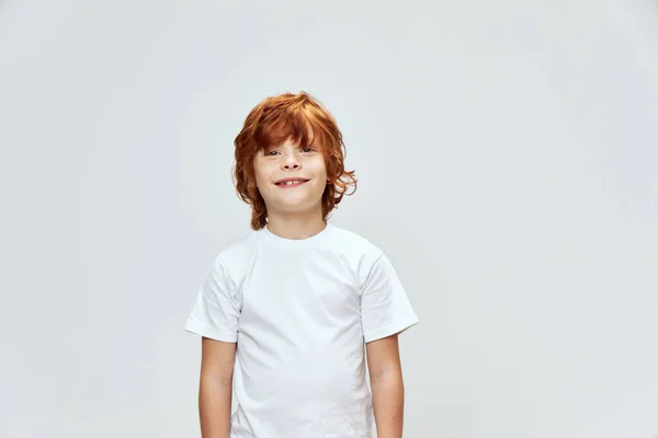 Glimlachende roodharige jongen in wit t-shirt op zoek boven grijze studio achtergrond — Stockfoto