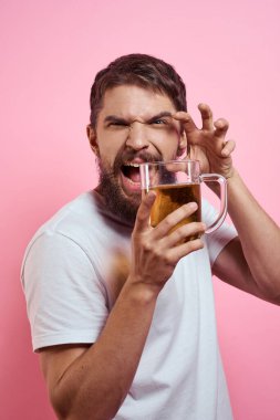 Pembe arka planda bira kupasıyla sakallı bir adam. Eğlenceli duygular beyaz tişörtlü sarhoş bir adamın görüntüsünü engelledi.