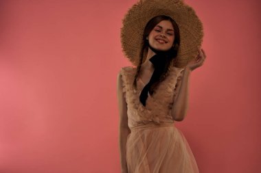 Pembe arka planda siyah kurdeleli şık elbiseli ve şapkalı bir kadın model duygularının eğlenceli görüntüsünü kırptı.