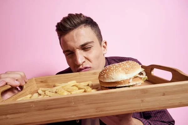 ファーストフードのある男食べるハンバーガーフライドポテトピンクの背景 — ストック写真