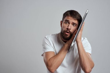 Elinde dizüstü bilgisayarla beyaz tişörtlü bir arka planı olan bir adamın duyguları yeni teknolojileri aydınlatır.