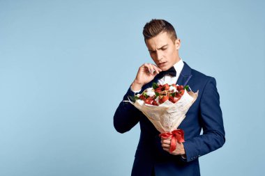Bir buket çiçekli ve mavi arka planda papyonlu romantik bir adam.
