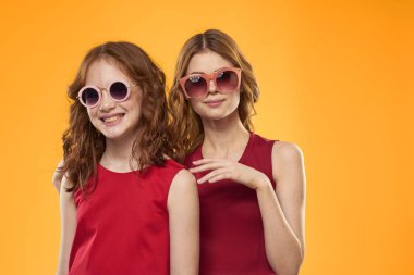 Kırmızı elbiseli mutlu kadın ve küçük kız sarı arka planda eğleniyorlar. Moda duyguları kız kardeşler gibi eğleniyorlar..