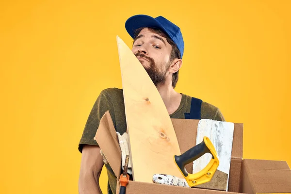 Egy ember munkaformában egy doboz betöltő szerszámok sárga háttér — Stock Fotó