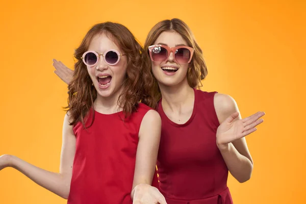 Hermanas felices en vestidos rojos sobre un fondo amarillo se están divirtiendo y gesticulando Copy Space — Foto de Stock