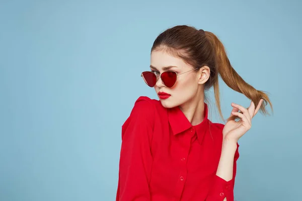 Woman in red shirt on blue background holds hands near face and sunglasses red lips makeup model — Stock Photo, Image