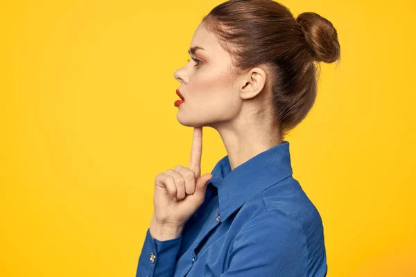 Retrato de uma mulher em uma camisa azul com maquiagem brilhante lábios vermelhos fundo amarelo vista recortada — Fotografia de Stock