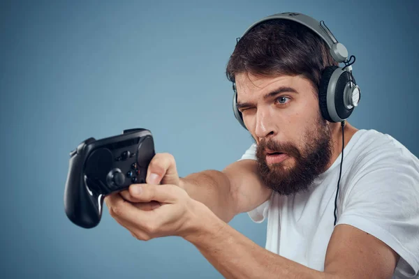 Hombre en auriculares controlador en las manos jugando consola estilo de vida emociones azul fondo blanco camiseta —  Fotos de Stock