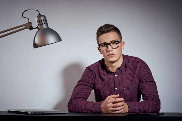 Homem de negócios com óculos e uma camisa sentada a uma mesa em um quarto escuro com uma lâmpada vista cortada — Fotografia de Stock