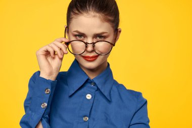 Mavi gömlekli, gözlüklü, yüzünde parlak makyajlı bir kadın elleriyle işaret ediyor.