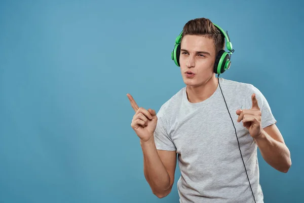 Ο άνθρωπος με πράσινα ακουστικά ακούει μουσική ψυχαγωγία lifestyle λευκό t-shirt μπλε φόντο — Φωτογραφία Αρχείου