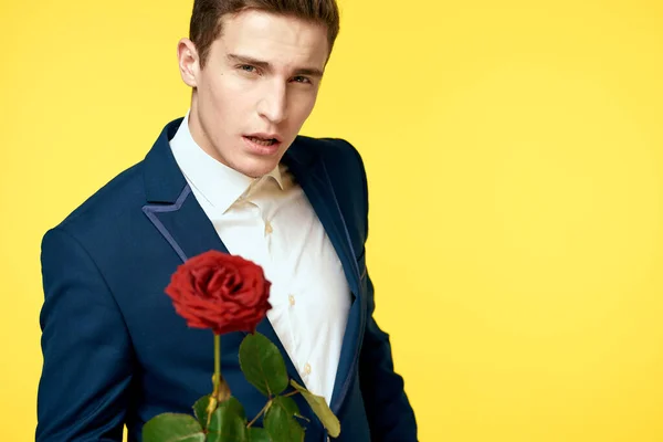 Jeune homme en costume classique avec une rose rouge à la main sur un fond jaune émotions recadré modèle de vue — Photo