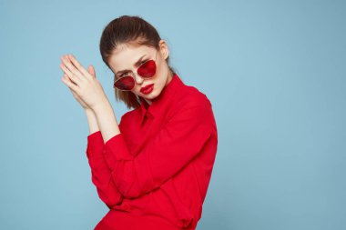 Mavi arka plandaki kırmızı gömlekli kadın yüz ve güneş gözlüklü kırmızı dudak makyajı modeli ile el ele tutuşuyor.