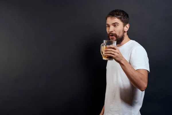 Homme avec une tasse de bière dans ses mains émotions style de vie amusant t-shirt blanc fond sombre isolé — Photo