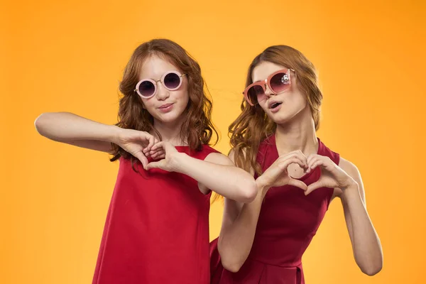 Mulher feliz e menina em vestido vermelho estão se divertindo em um fundo amarelo emoções da moda irmãs diversão espaço de cópia. — Fotografia de Stock