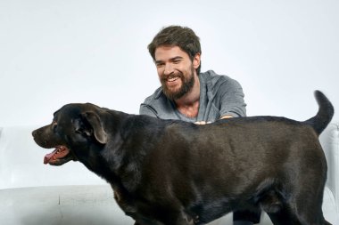 Erkek sahibi kanepede köpekle oynuyor. Eğlenceli ışık odası arkadaşları evcil hayvanı eğitiyor.