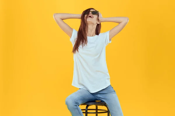 Pretty woman sits on a chair wearing sunglasses yellow background lifestyle — Stock Photo, Image