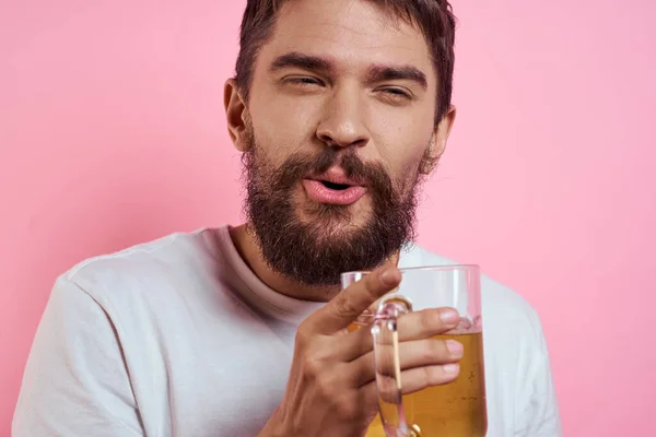 Homem barbudo com uma caneca de cerveja Em um fundo rosa emoções divertidas vista cortada de uma camiseta branca bêbado — Fotografia de Stock