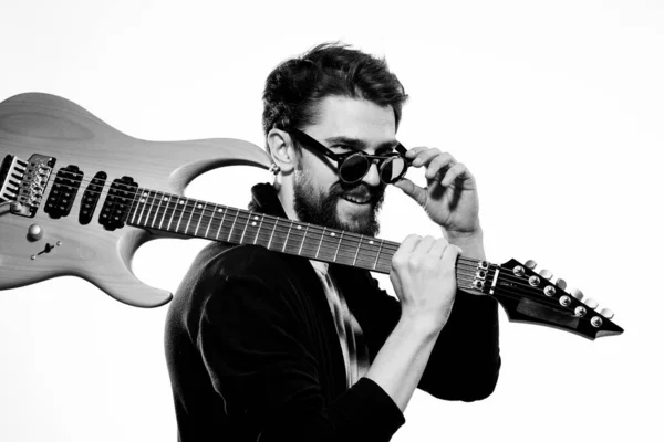 Um homem segura uma guitarra em suas mãos jaqueta de couro preto óculos escuros performance musical luz de fundo — Fotografia de Stock