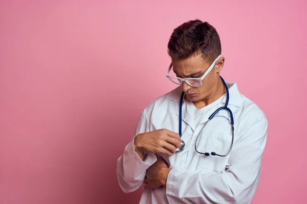 Médecin masculin en robe médicale avec un stéthoscope autour du cou sur un fond rose et des lunettes sur le visage — Photo