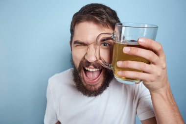 Beyaz tişörtlü, bira kupalı, sarhoş, mavi arka planlı neşeli bir adam.
