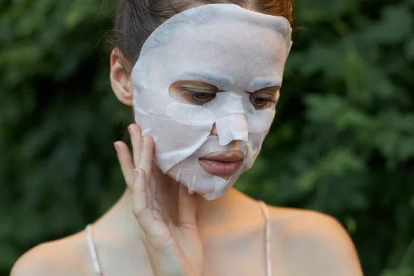 Wanita cantik masker wajah menyentuh wajah Anda dengan tangan Anda kosmetologi daun di latar belakang — Stok Foto