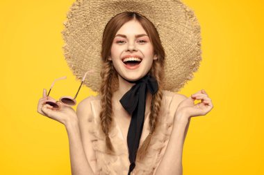Şapkalı romantik bir kadın sarı arka planda eğleniyor ve güneş gözlüğü siyah kurdele modeli portresi takıyor.