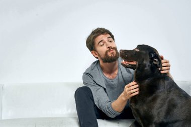 Erkek sahibi kanepede köpekle oynuyor. Eğlenceli ışık odası arkadaşları evcil hayvanı eğitiyor.