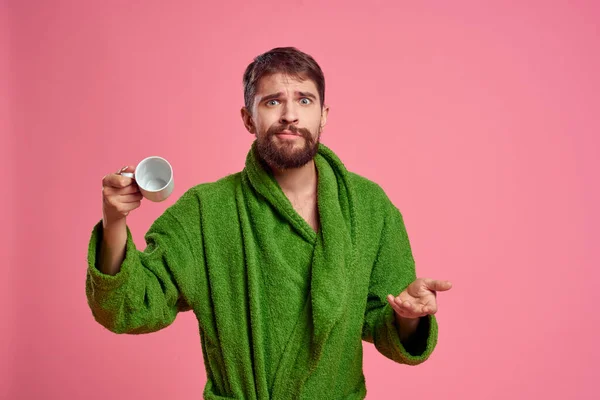 Человек с чашкой чая на розовом фоне обрезанный вид эмоций модели зеленый халат — стоковое фото