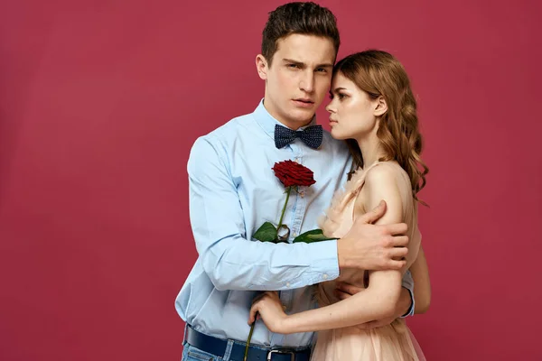 Enamored man and woman with a red flower on a pink background hug each other Copy Space — Stock Photo, Image