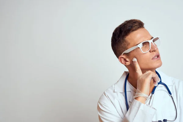 Médecin dans une robe médicale avec un stéthoscope et des lunettes sur un fond clair portrait de vue recadrée — Photo