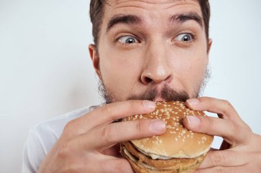 Beyaz bir tişörtle arka planda hamburger yiyen bir adam yakın çekim açlık ve fast food manzarası izledi.