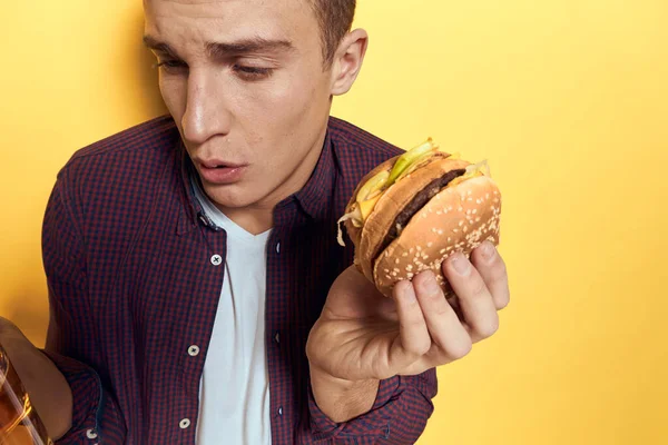 Fröhlicher Mann mit einem Becher Bier und einem Hamburger an den Händen Diät-Lebensstil gelber Hintergrund — Stockfoto