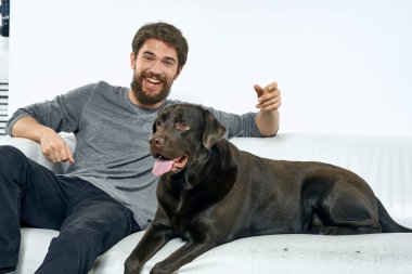 Beyaz bir kanepede siyah köpeği olan bir adam. Arka planda, yakın planda kesilen evcil hayvan insan arkadaş duyguları. Eğlenceli.