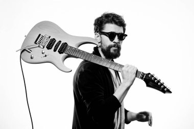 Elinde bir gitar tutan bir adam. Siyah deri ceket. Siyah gözlükler.
