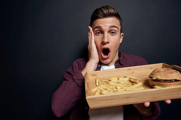 Muž drží dřevěnou paletu s rychlým občerstvením v ruce strava jídlo hlad životní styl tmavé pozadí — Stock fotografie