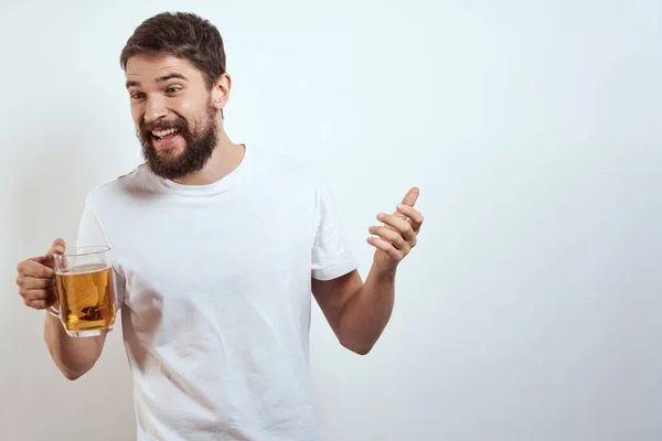 Hombre con una taza de cerveza en sus manos y una camiseta blanca fondo claro bigote barba emociones modelo —  Fotos de Stock