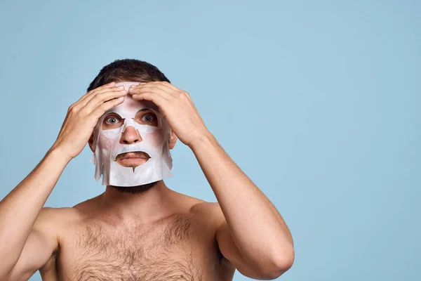 man in cleansing mask on blue background gesturing with hands naked torso cropped view