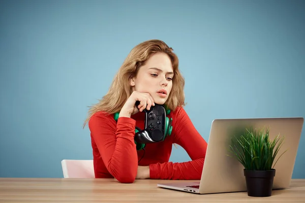 Mulher sentada em uma mesa na frente de um controlador de fones de ouvido laptop jogando estilo de vida on-line fundo azul — Fotografia de Stock