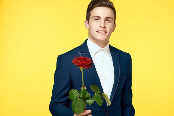 Young man in a classic suit with a red rose in his hand on a yellow background emotions cropped view model — Stock Photo, Image