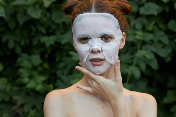 Hermosa mujer antiarrugas máscara en la naturaleza, toca su cara desnuda hombros arbustos en el fondo —  Fotos de Stock