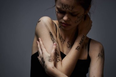 Vücudunda kızgın yazılar olan gücenmiş bir kadın gri bir arka plan saldırganlığıyla kendisine dokunuyor. 