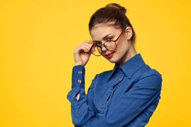 Mavi gömlekli, gözlüklü, yüzünde parlak makyajlı bir kadın elleriyle işaret ediyor.