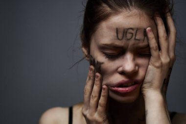 Gri arka planda kırıcı yazılar yazan üzgün kadın elleriyle kendine dokunuyor.