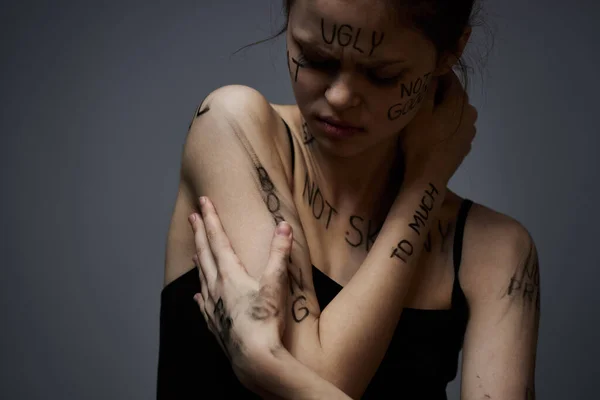 Προσβεβλημένη γυναίκα με θυμωμένες επιγραφές στο σώμα της αγγίζει τον εαυτό της με τα χέρια της σε ένα γκρίζο φόντο επιθετικότητα — Φωτογραφία Αρχείου