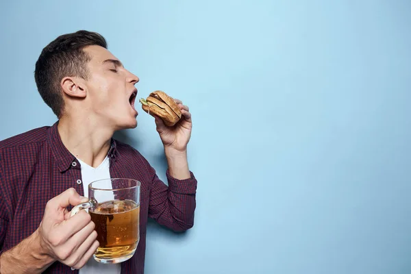 Bira bardağı ve hamburgerli neşeli sarhoş adam. Diyet yemek yaşam tarzı mavi arka plan. — Stok fotoğraf