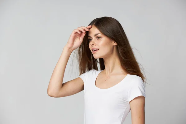 Beautiful woman holds her hands near her face and looks to the side in a white t-shirt — Stock Photo, Image