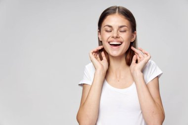 Neşeli kadın gülümsüyor, gözleri kapalı beyaz tişört giyiyor. 